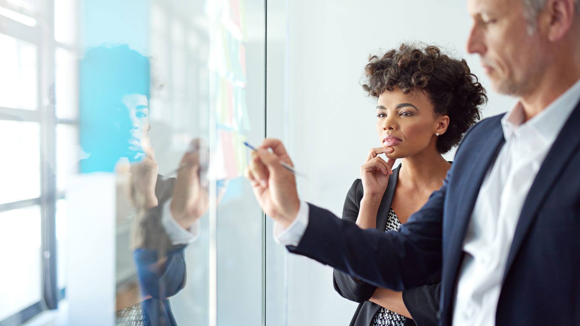 Two professionals reviewing ideas on a glass board during a collaborative strategy session.