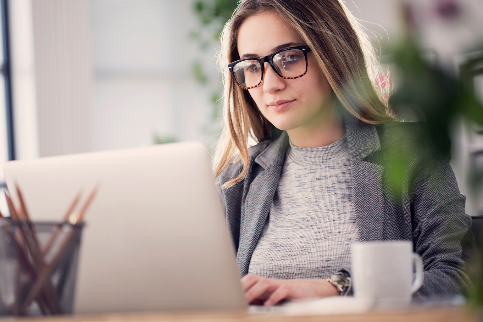 white female in glasses looking at a laptop screen