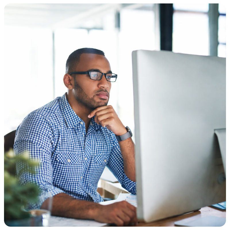 black young male in glasses looking at a computer monitor